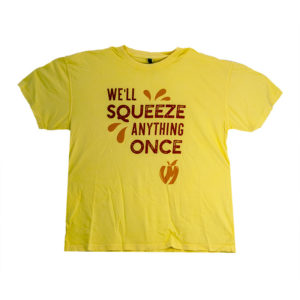Pale yellow t-shirt with "We'll squeeze anything once" in red with bright orange design elements surrounding the text including a VM apple logo